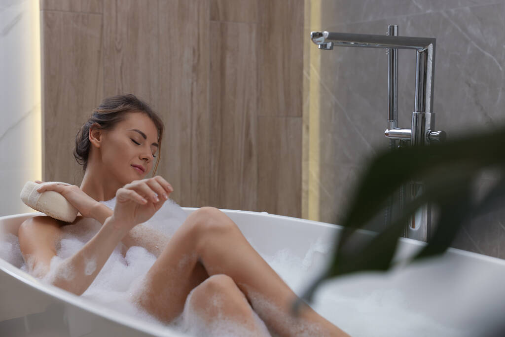 Женщина с губкой, принимающая ванну в помещении, место для текста - Фото, изображение