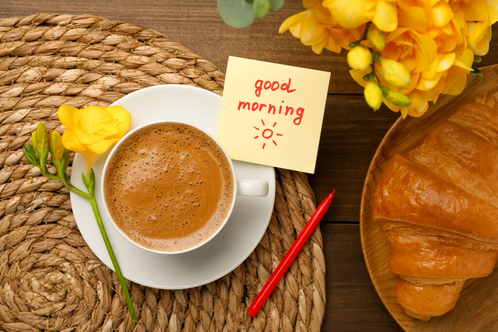 Cup of aromatic coffee with croissant, beautiful yellow freesias and Good Morning note on wooden table, flat lay - Photo, Image
