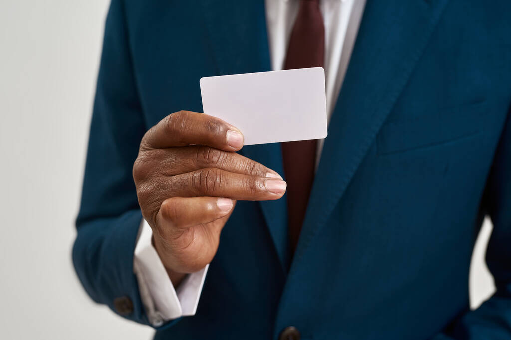 Κοντινό πλάνο της επαγγελματικής κάρτας στο χέρι του μαύρου επιχειρηματία. Περικοπή εικόνα του ανθρώπου που φοράει επίσημη ένδυση. Έννοια του σύγχρονου επιτυχημένου ανδρικού τρόπου ζωής. Απομονωμένο σε λευκό φόντο. Στούντιο σουτ - Φωτογραφία, εικόνα