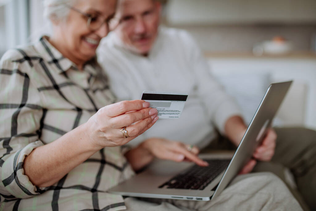 Kanepede oturan ve internetten bilgisayar ve kredi kartıyla alışveriş yapan yaşlı bir çift. - Fotoğraf, Görsel