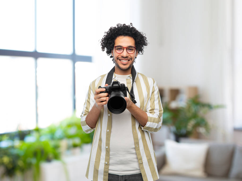 fotografie, profese a lidé a koncept - šťastný usmívající se muž nebo fotograf v brýlích s digitálním fotoaparátem nad domácím pokojem pozadí - Fotografie, Obrázek