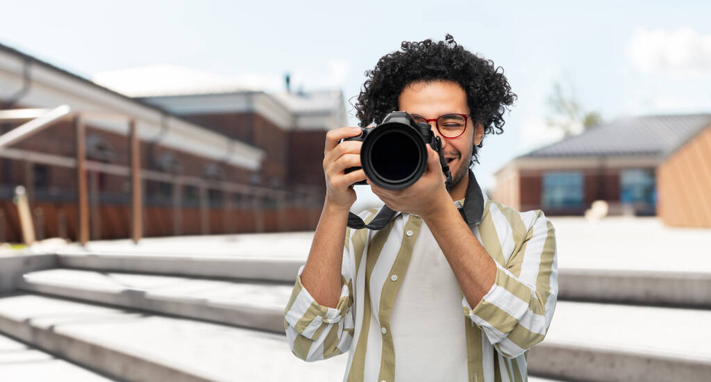 fotografie, beroep en mensen en concept - vrolijke glimlachende man of fotograaf in bril met digitale camera over stadsstraatachtergrond - Foto, afbeelding
