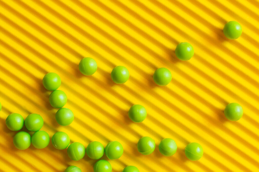 vista superior de pequeñas bolas verdes dispersas sobre fondo amarillo texturizado - Foto, Imagen