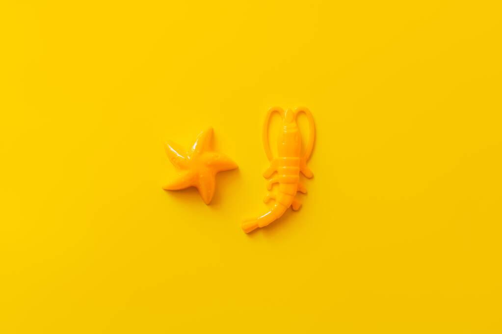 vista superior de camarones de plástico brillante y estrellas de mar sobre fondo amarillo - Foto, imagen