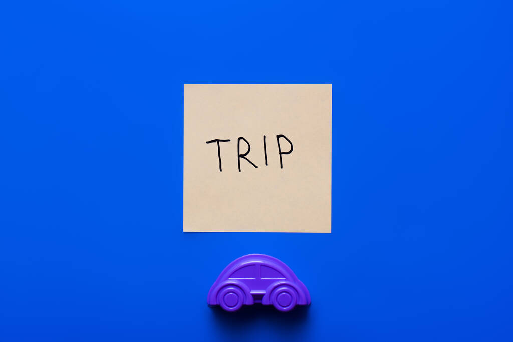 vue du haut de la carte de papier avec lettrage voyage près de voiture jouet violet sur fond bleu - Photo, image