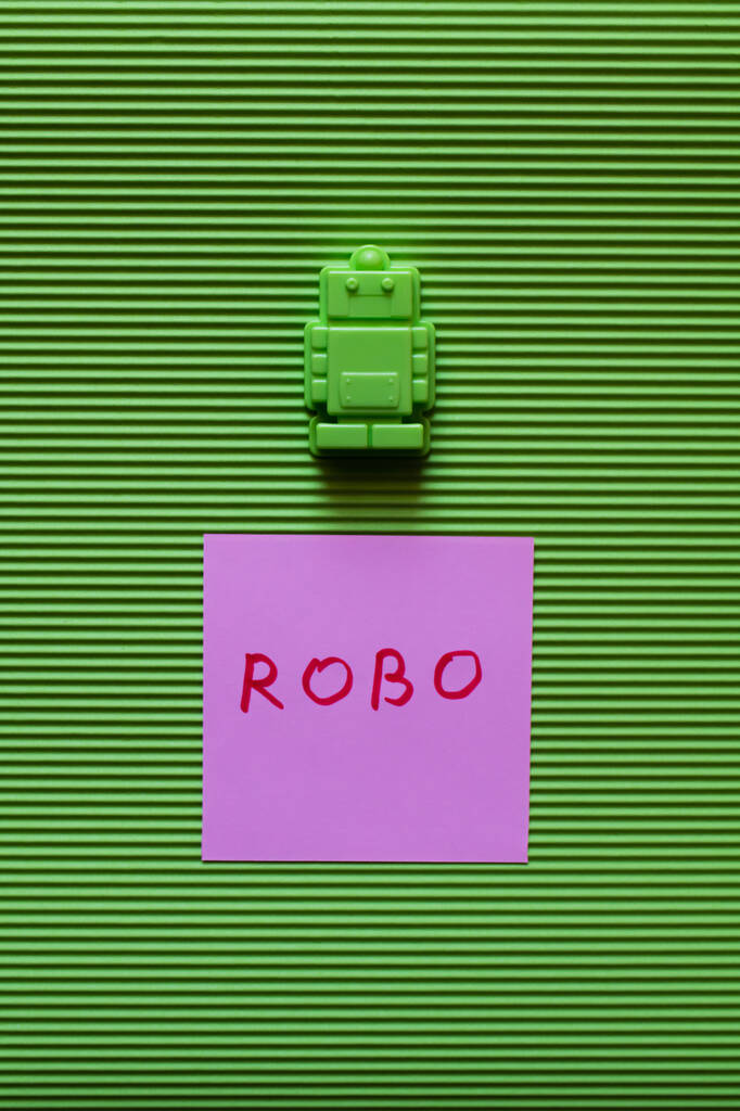 紫色の紙の近くのプラスチック製のおもちゃのトップビュー緑の背景にロボットの碑文 - 写真・画像