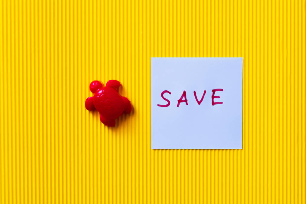 vista superior de la tortuga de juguete rojo cerca del papel con letras de guardar en el fondo amarillo texturizado - Foto, Imagen