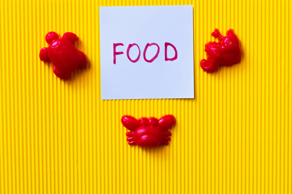 верхний вид красных игрушек морских существ рядом с синей картой с пищевыми надписями на желтом фоне - Фото, изображение