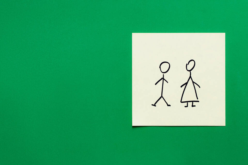 緑色の背景にオスとメスのアイコンが描かれた紙のカードの上からの眺め - 写真・画像