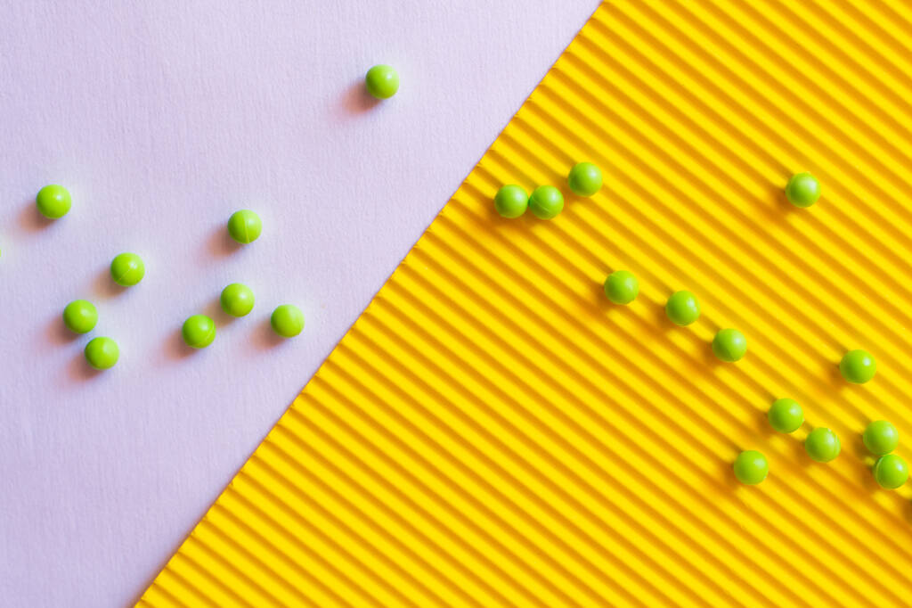 вид сверху на маленькие зеленые шарики на фиолетовом и желтом текстурированном фоне - Фото, изображение