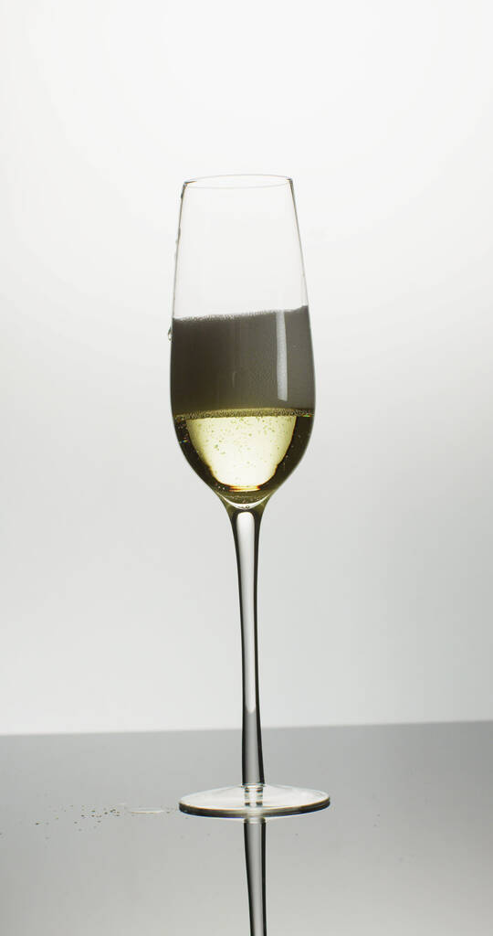 Вертикальное изображение открытой бутылки, наливающей шампанское в одиночный тюльпановый бокал на белом фоне. роскошь, отдых и праздник. - Фото, изображение