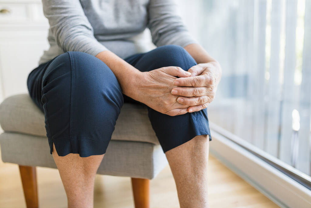 Старшая женщина дома держит больное колено - Фото, изображение