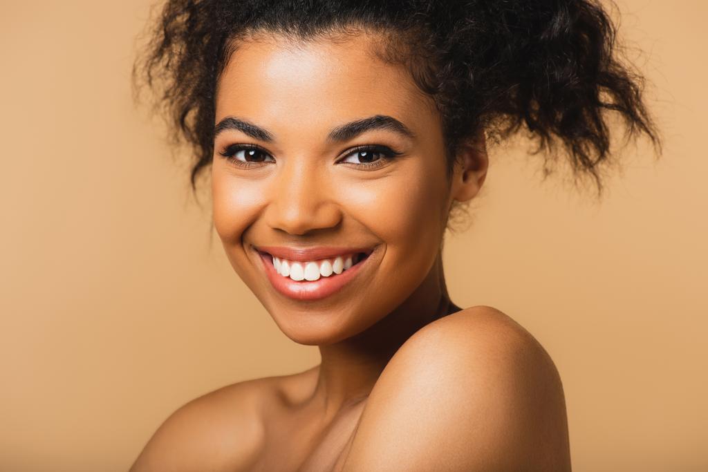 retrato de alegre mujer afroamericana con hombros desnudos y piel perfecta aislada en beige  - Foto, Imagen