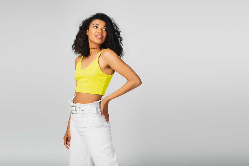 pretty african american woman in yellow crop top posing with hand on hip isolated on grey - Photo, Image
