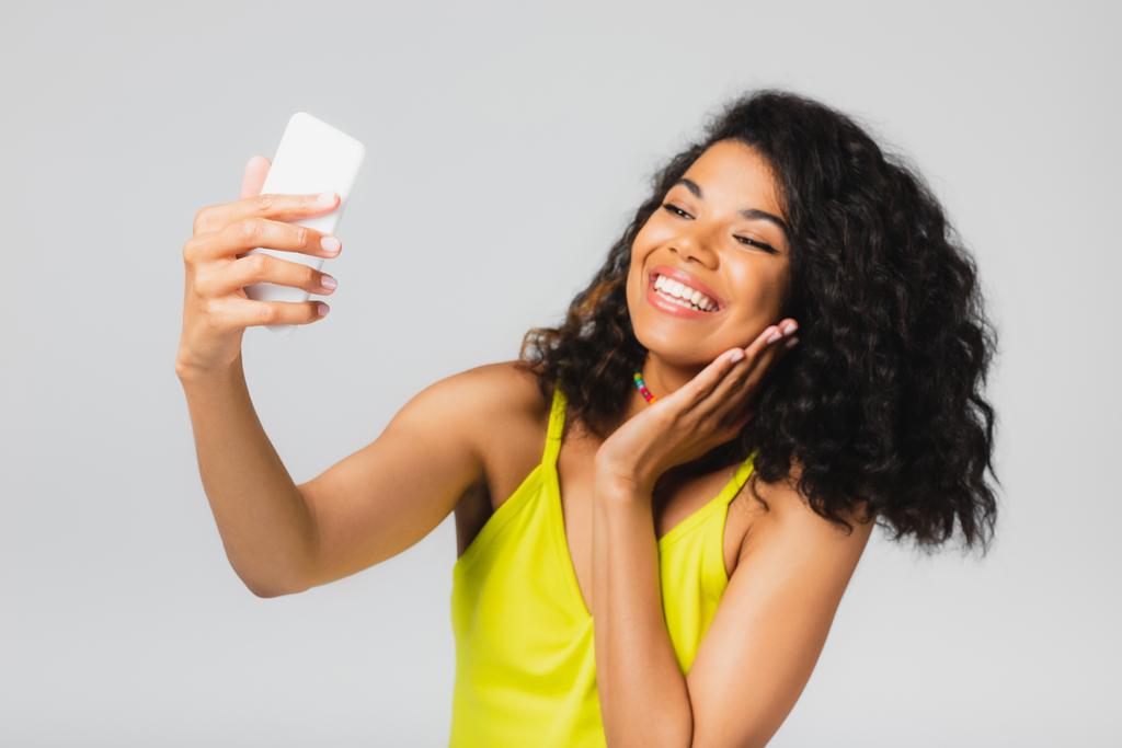 felice donna afro-americana scattare selfie su smartphone isolato su grigio  - Foto, immagini
