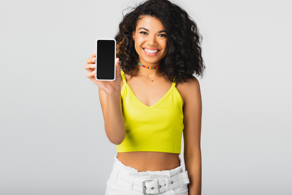 vidám afro-amerikai nő gazdaság smartphone üres képernyő elszigetelt szürke  - Fotó, kép