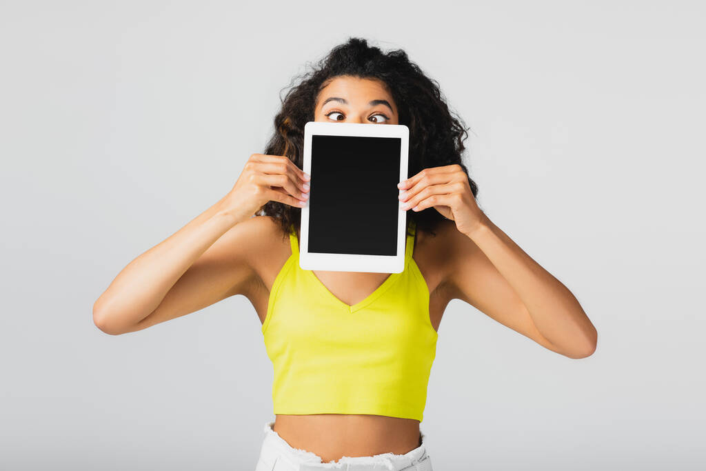 mulher americana africana encaracolado no topo da cultura amarela segurando tablet digital com tela em branco isolado em cinza - Foto, Imagem