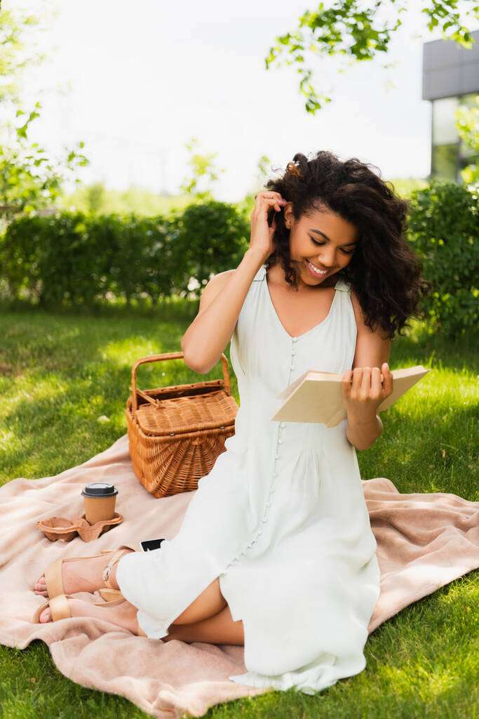 veselé africké Američanky v šatech čtení román a sedí na dece v parku - Fotografie, Obrázek
