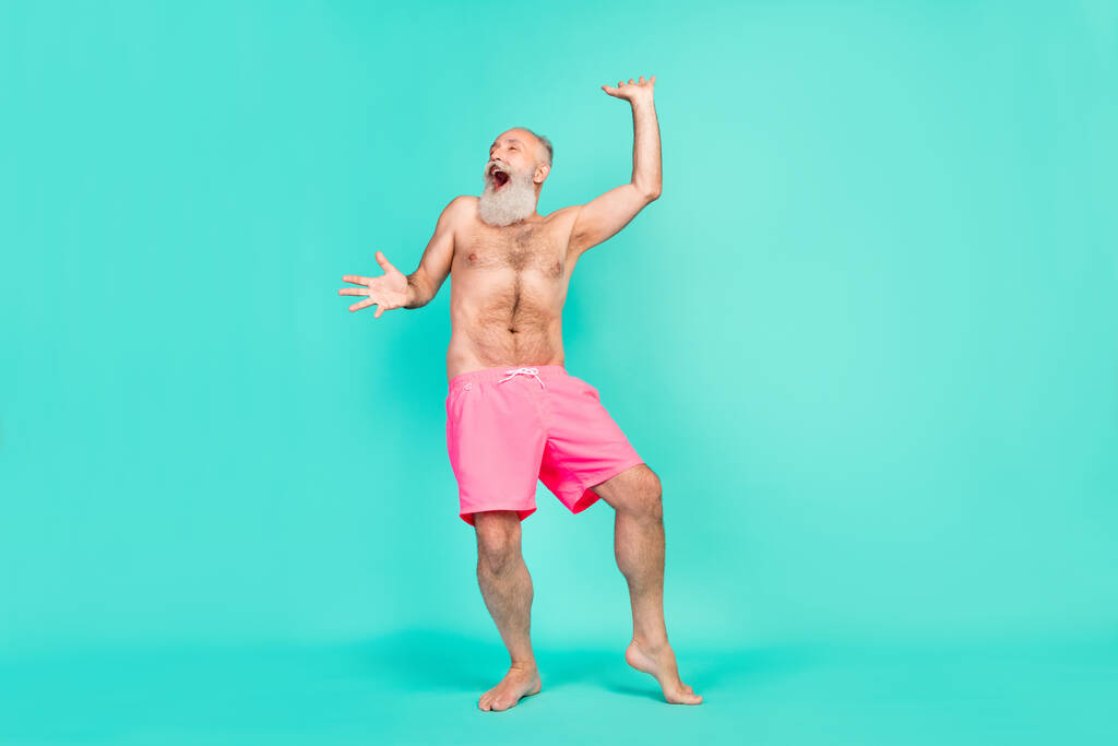 Zdjęcie szalony nieostrożny stary człowiek taniec plaża party krzyk radować nosić różowe szorty odizolowane turkusowe tło kolor. - Zdjęcie, obraz