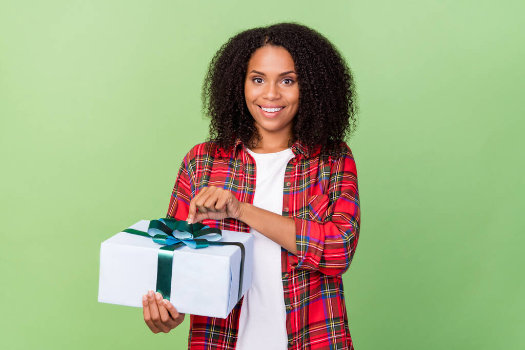 Photo of young cheerful african woman open present box ribbon season isolated over green color background. - Photo, Image