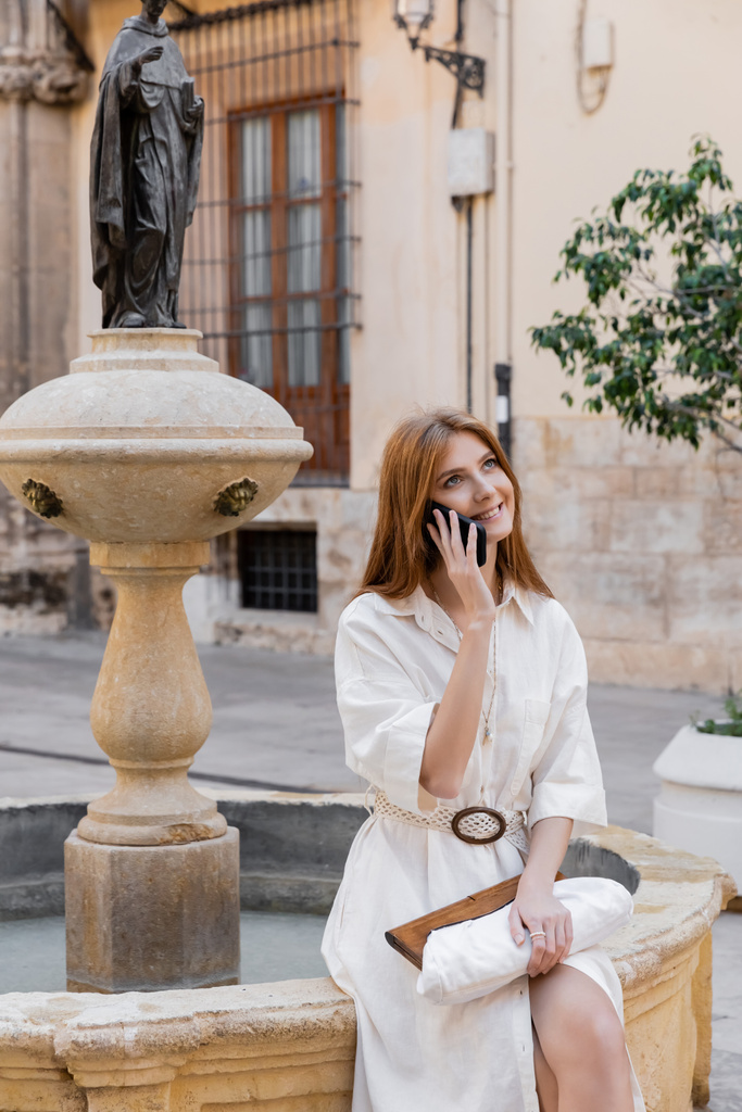χαρούμενη γυναίκα σε λευκό φόρεμα μιλάμε για smartphone κοντά στο σιντριβάνι σε valencia - Φωτογραφία, εικόνα