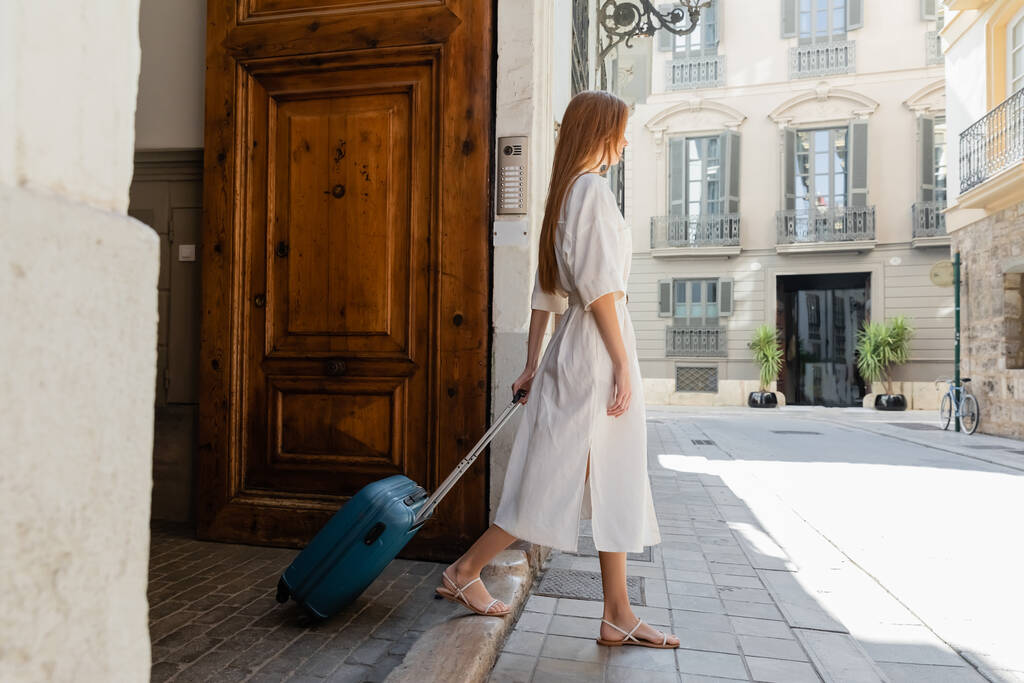 volledige lengte van jonge vrouw in jurk wandelen met bagage op Europese straat - Foto, afbeelding