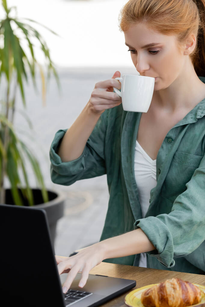 młoda kobieta z czerwonymi włosami przy użyciu laptopa i picia kawy w kawiarni taras - Zdjęcie, obraz