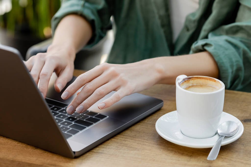 Kafe terasında bir fincan kahvenin yanında dizüstü bilgisayar kullanan bir kadın görüntüsü. - Fotoğraf, Görsel