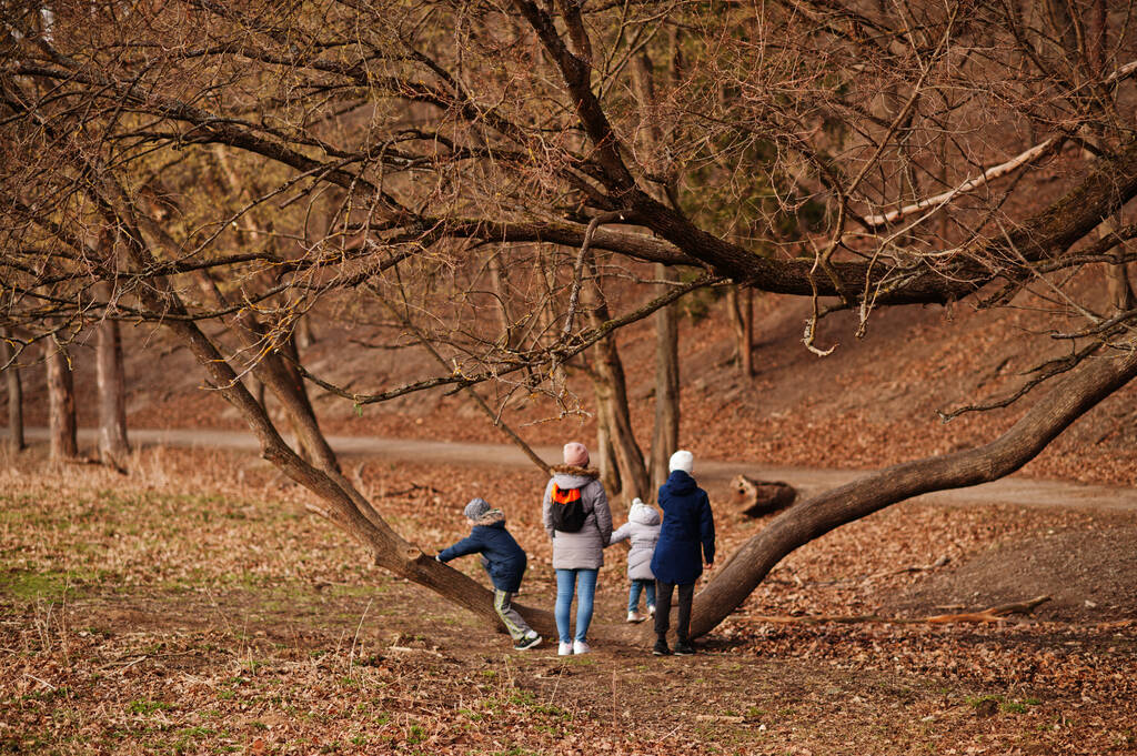 Az anya háta négy gyerekkel zakót és kalapot visel a kora tavaszi erdőben.. - Fotó, kép