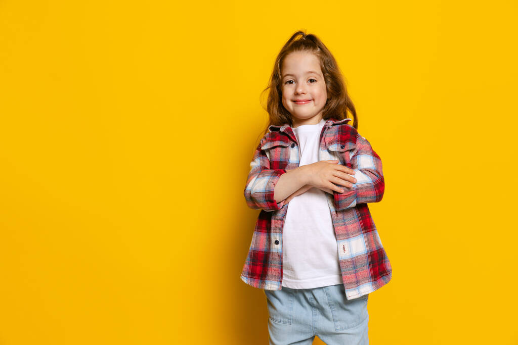 Memnun görünüyor. Mutlu küçük kız, parlak sarı arka planda izole edilmiş sıcak ekose gömlek giyen çocuk. Çocuk duyguları, moda, güzellik, okul ve reklam kavramı. Çocuk modası, sokak tarzı. - Fotoğraf, Görsel