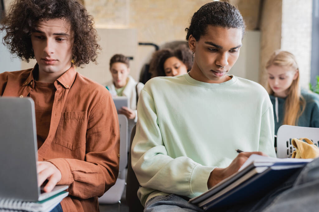 afro-amerikai diák írás notebook, miközben barátja gépelés a laptopon a lecke alatt - Fotó, kép