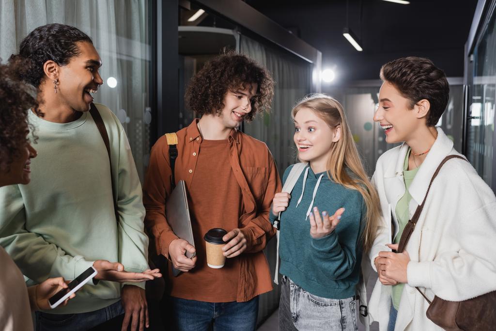veselí multikulturní studenti mluví a gestikulují na univerzitní chodbě - Fotografie, Obrázek