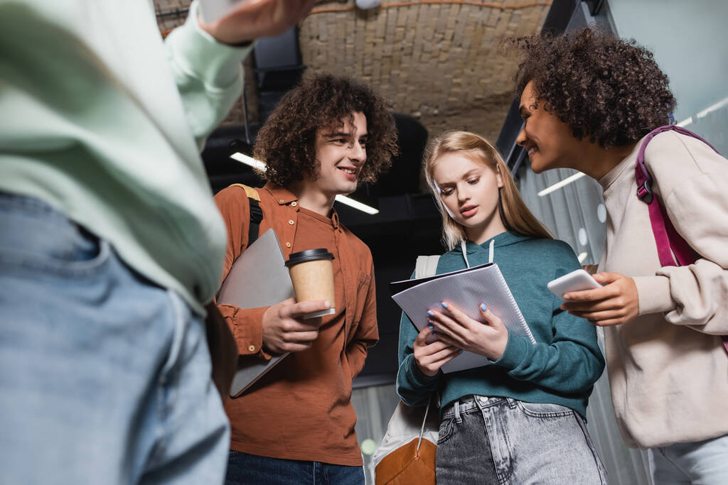 Low-Winkelansicht multiethnischer Studenten mit Gadgets, Coffee to go und Notizbuch - Foto, Bild