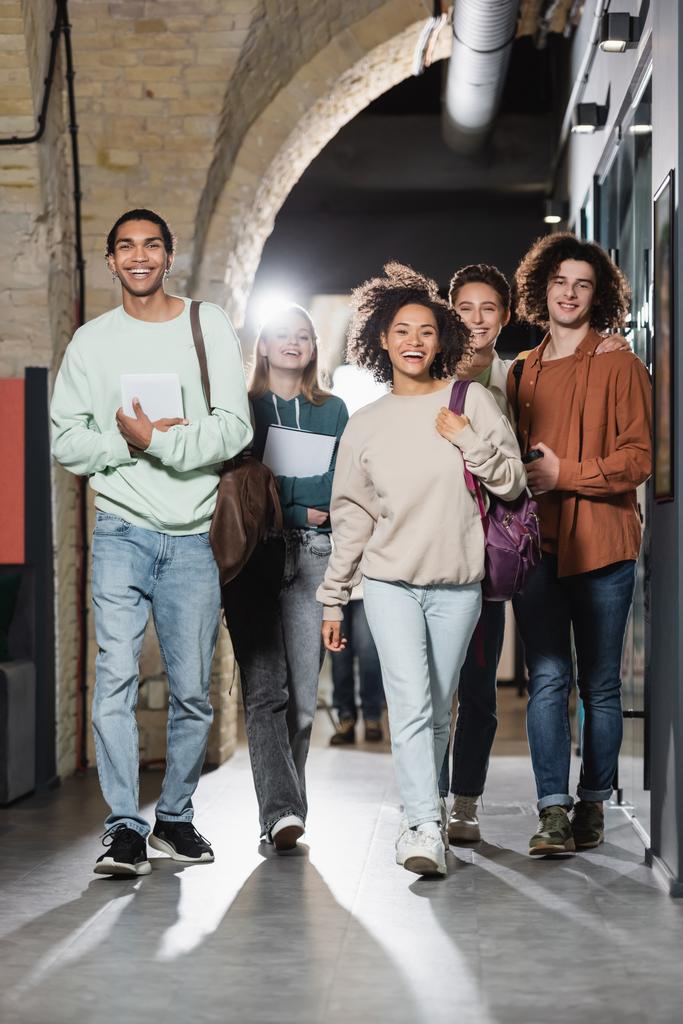 a folyosón sétáló és a kamerába bámuló vidám, többnemzetiségű diákok teljes hossza - Fotó, kép