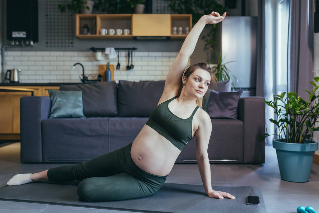Young beautiful pregnant woman at home doing fitness sitting on the floor - Photo, Image