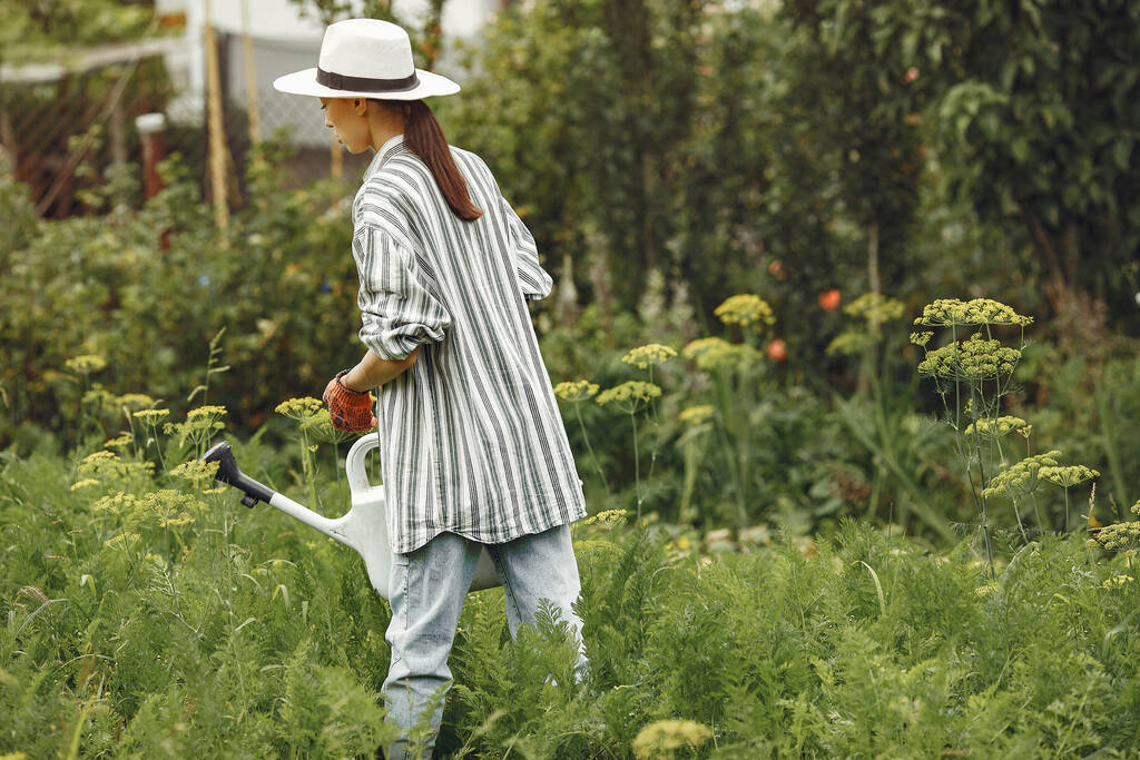 Kertészkedés nyáron. A nő öntözi a virágokat egy öntözőkannával. Sapkát viselő lány. - Fotó, kép