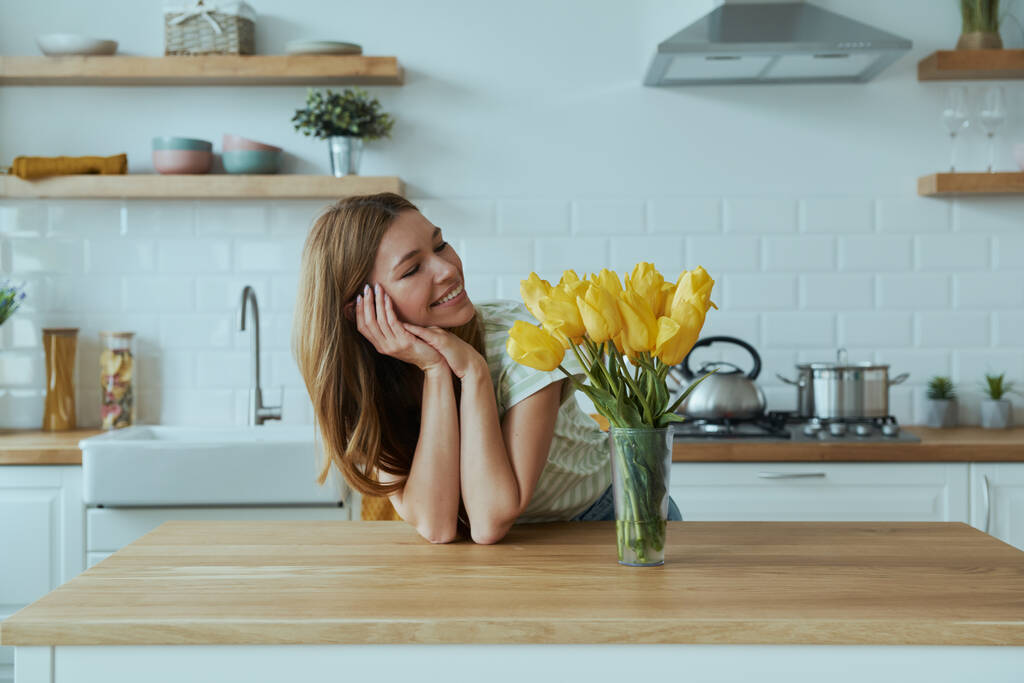 gelukkig jong vrouw leunend aan de keuken bureau en glimlachen - Foto, afbeelding