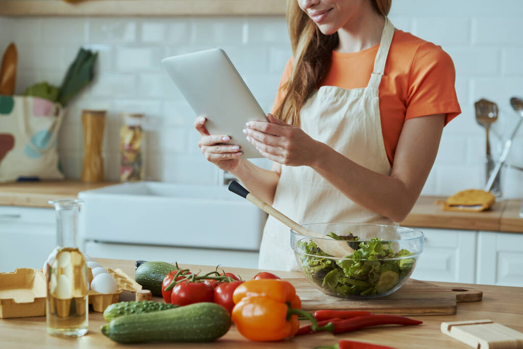 Közelkép magabiztos nő használ digitális tabletta főzés közben a háztartási konyhában - Fotó, kép
