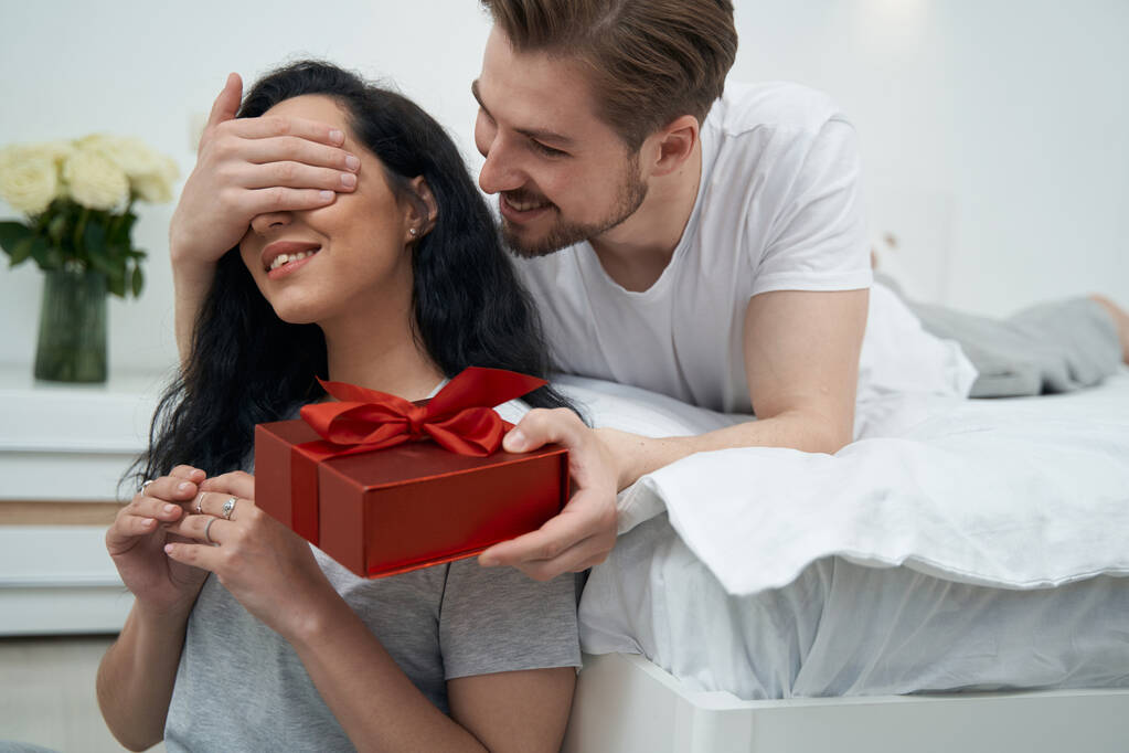 Веселий хлопець дарує подарунок задоволеній леді, прикриваючи очі рукою
 - Фото, зображення