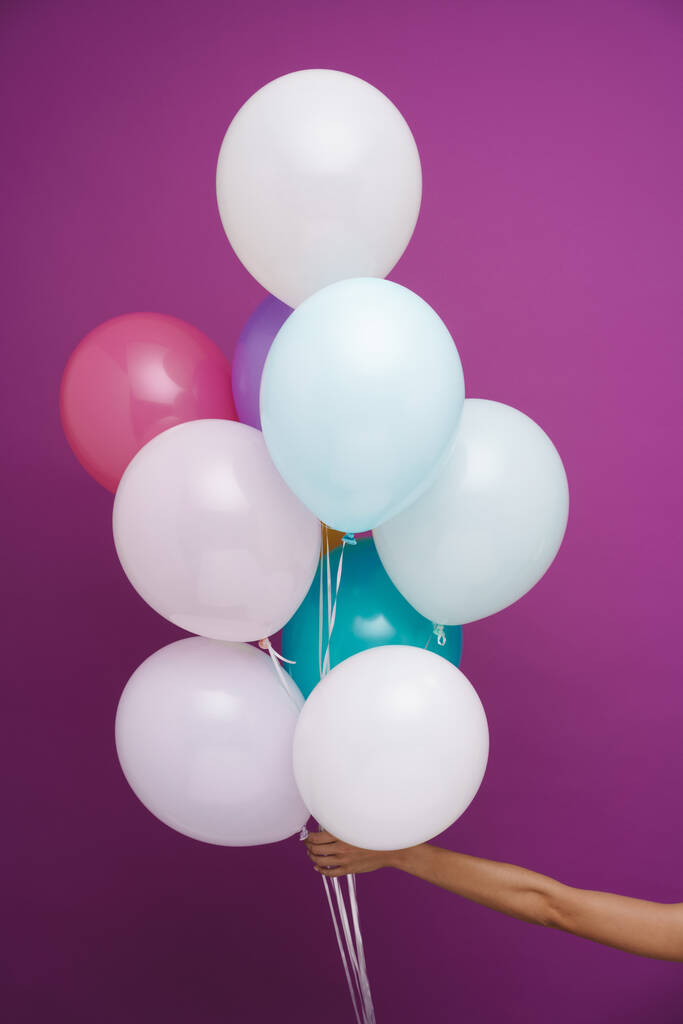Fotografie ženské ruky zobrazující mnohobarevné balónky izolované přes fialové pozadí - Fotografie, Obrázek