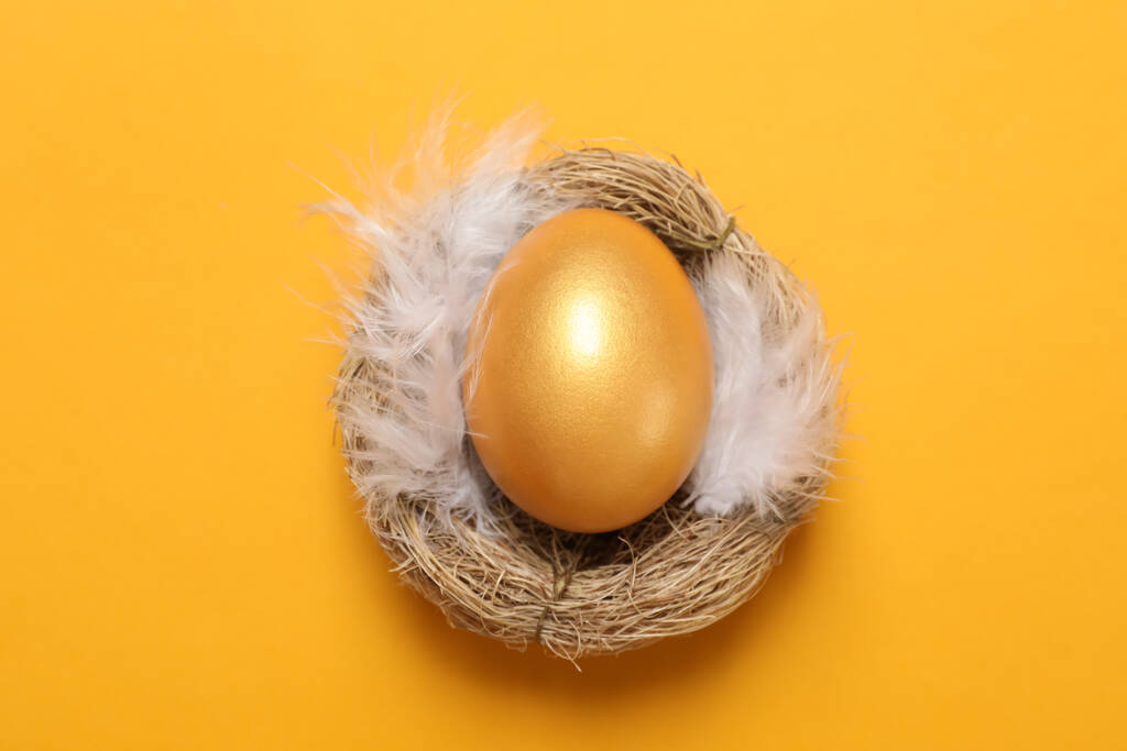 Fényes arany tojás tollak fészekben narancssárga háttér, felső nézet - Fotó, kép