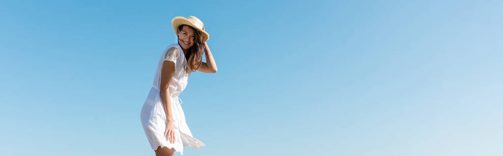 Nuori nainen valkoisessa mekossa ja aurinkohattu hymyilee kameralle taivas taustalla, banneri  - Valokuva, kuva