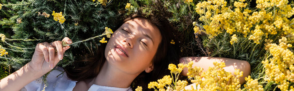 Κάτοψη της μελαχρινής γυναίκας ξαπλωμένη σε κίτρινα λουλούδια την ημέρα, πανό  - Φωτογραφία, εικόνα