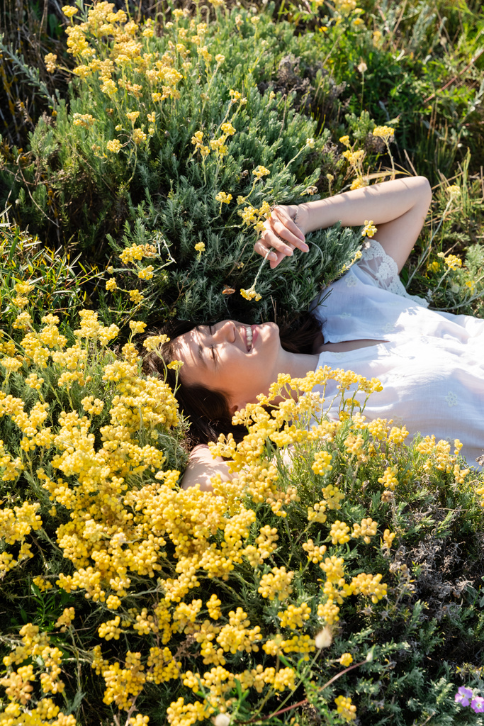 Wysoki kąt widzenia wesołej kobiety leżącej na trawniku z żółtymi kwiatami  - Zdjęcie, obraz