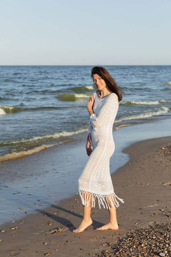 Barfüßige Frau in Strickkleid steht am Strand am Meer  - Foto, Bild
