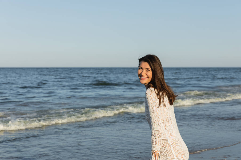 Happy brunette woman looking at camera near blurred sea  - Photo, Image