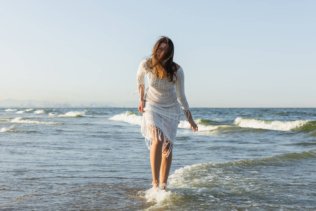 Morena mujer en vestido de pie en agua de mar  - Foto, imagen