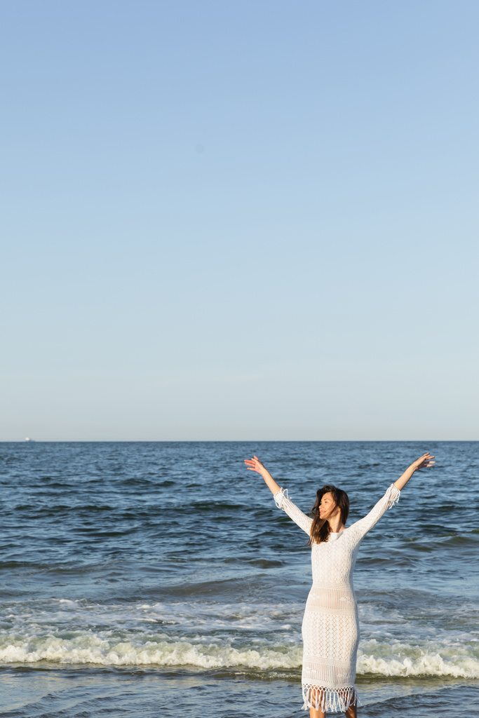 Mulher positiva em vestido de pé perto do mar com céu azul no fundo  - Foto, Imagem