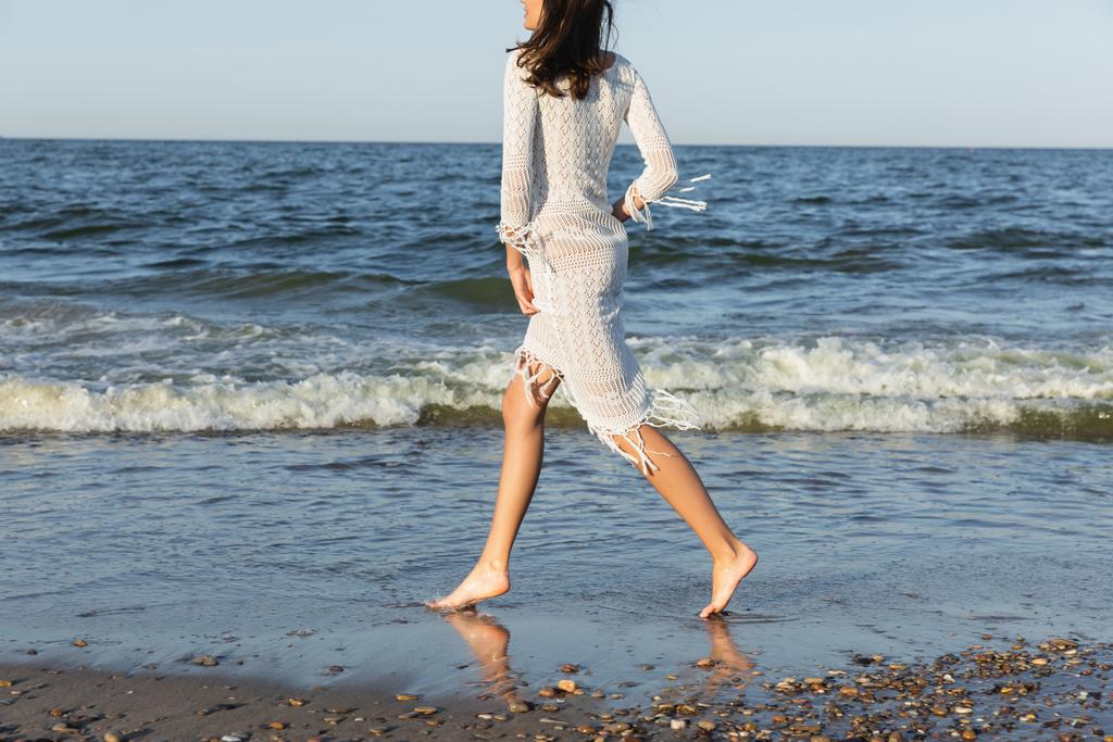 Gewassen uitzicht op brunette vrouw in jurk draait op nat zand in de buurt van zee  - Foto, afbeelding