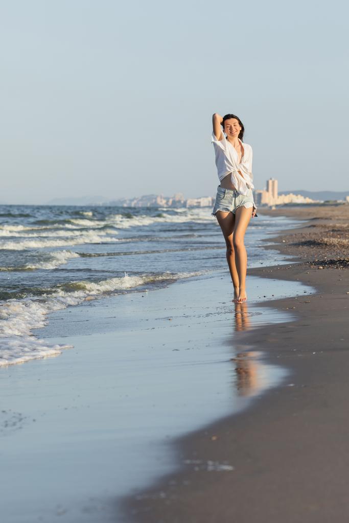 Όμορφη νεαρή γυναίκα με πουκάμισο και τζιν τζιν κοντά στη θάλασσα στην παραλία  - Φωτογραφία, εικόνα